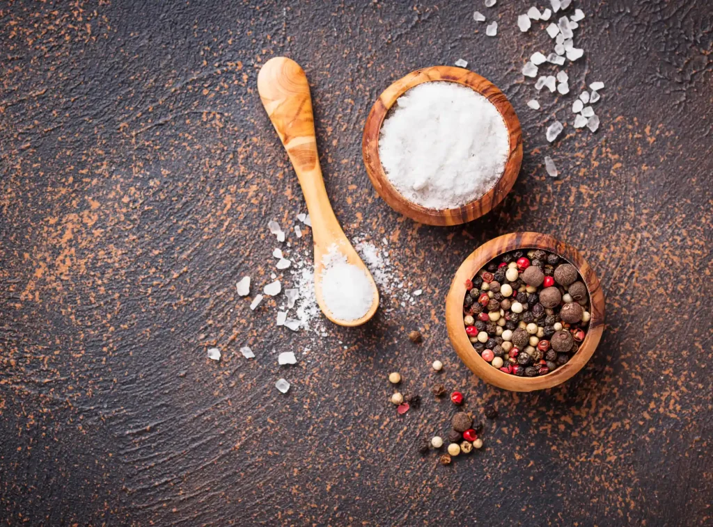 Bowls of salt and pepper on a copper surface before applying to jerky for a traditional beef jerky flavor.