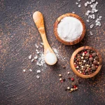 Bowls of salt and pepper on a copper surface before applying to jerky for a traditional beef jerky flavor.