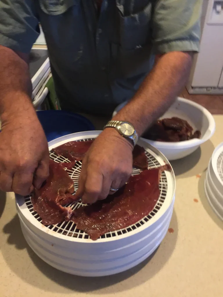 Homemade beef jerky being laid out in a dehydrator